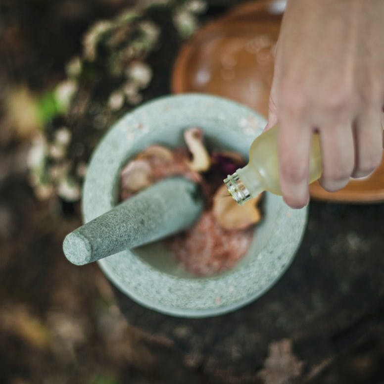 Someone pouring an oil into a mortar and pestle of flowers.
