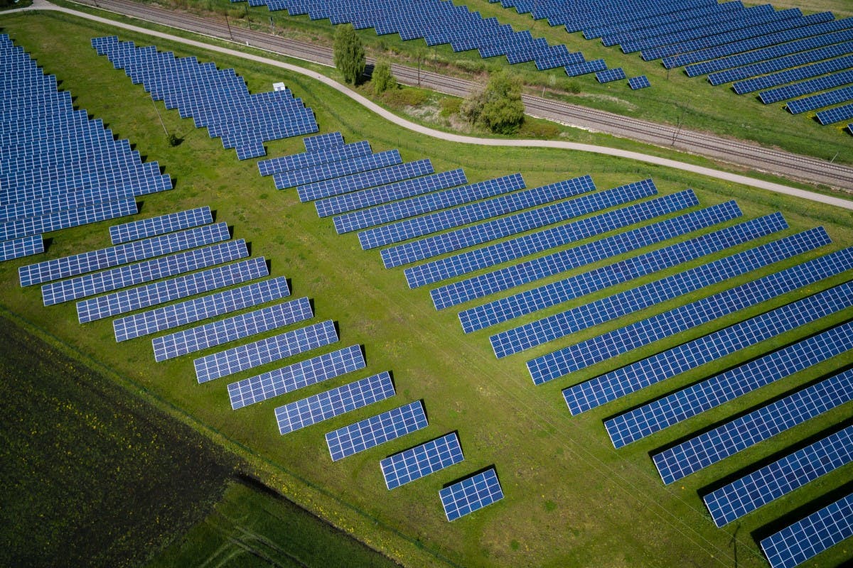 Aerial photo of a solar farm with solar panels layed out over green grass.