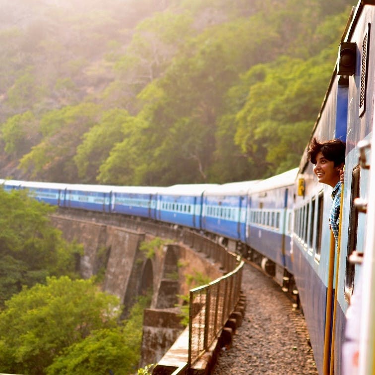 A lady pokes her head out of a train window to enjoy the view, as the train passes over a bridge. Travelling by train is a relaxing  and low emissions solution to travelling without without flying