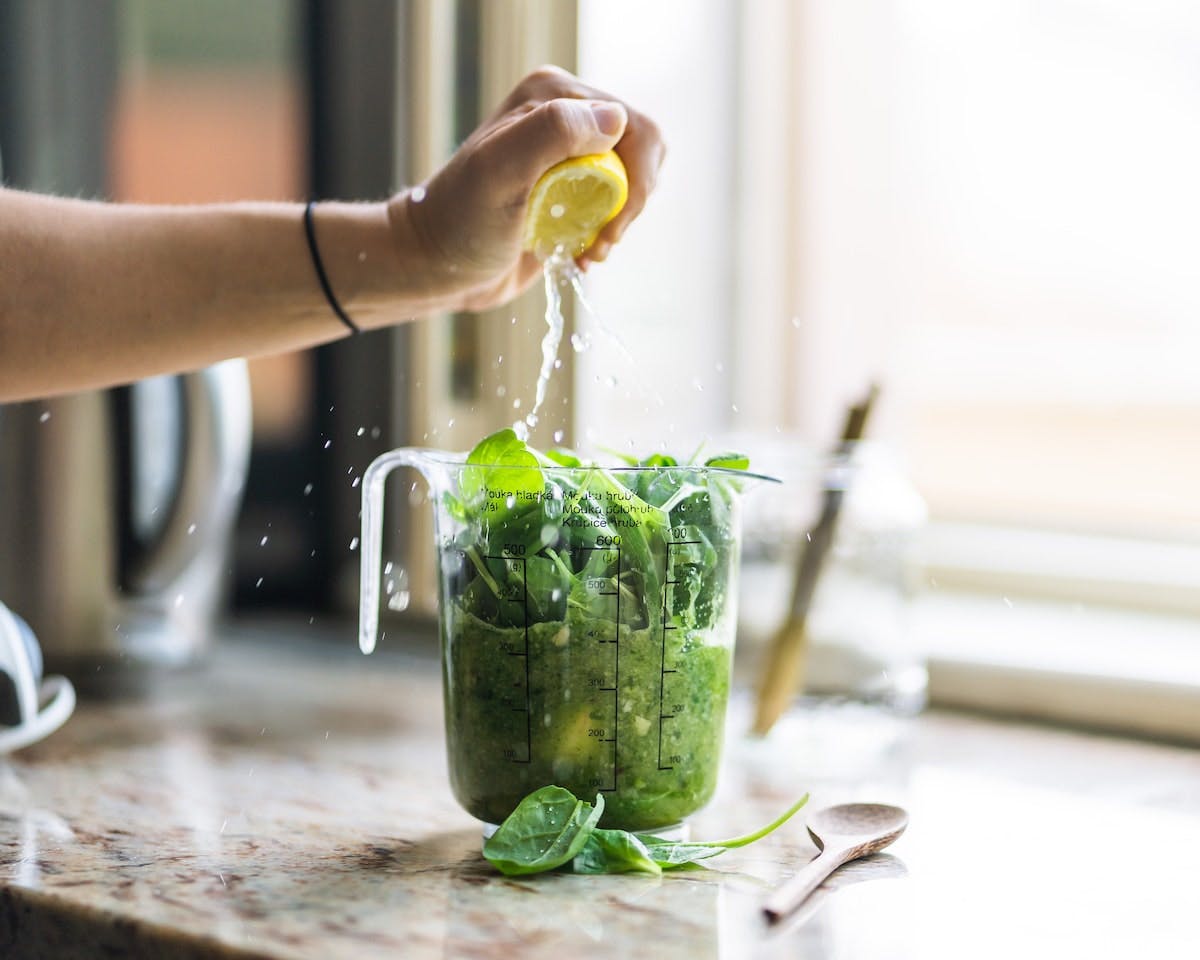 A person squeezing fresh lemon juice into their edible insect green smoothie.