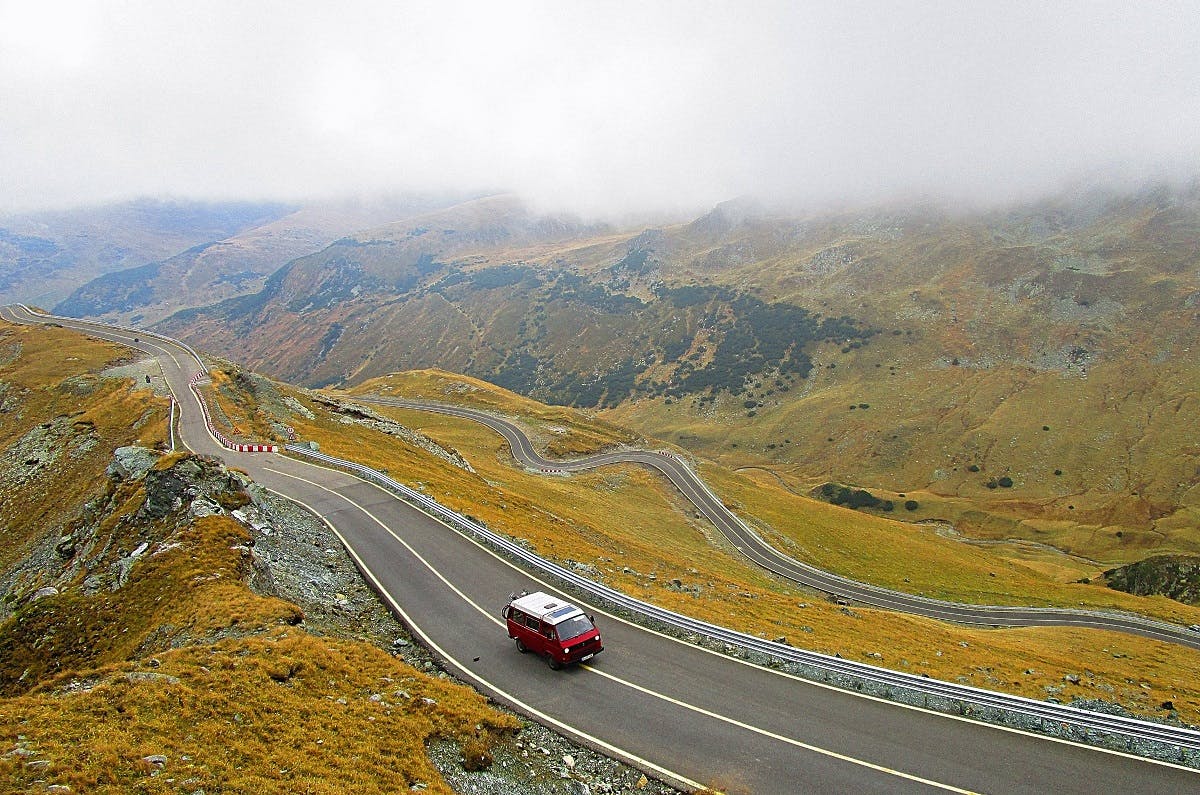 A red camper van out on the open road in beautiful mountains. Van life gives you an unrivalled sense of freedom. 