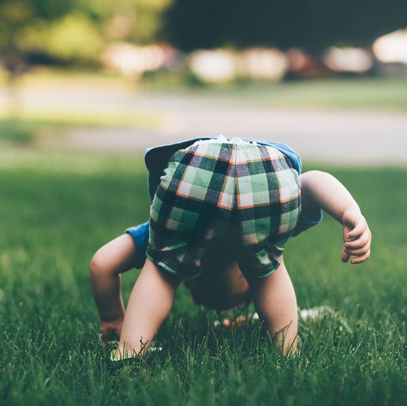 A toddler playing in the grass outside. Regular time in nature is a must when raising an eco baby.