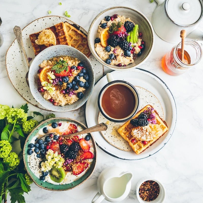 A delicious vegan breakfast comprising of porridge topped with fresh berries, waffles with honey and fresh ground coffee