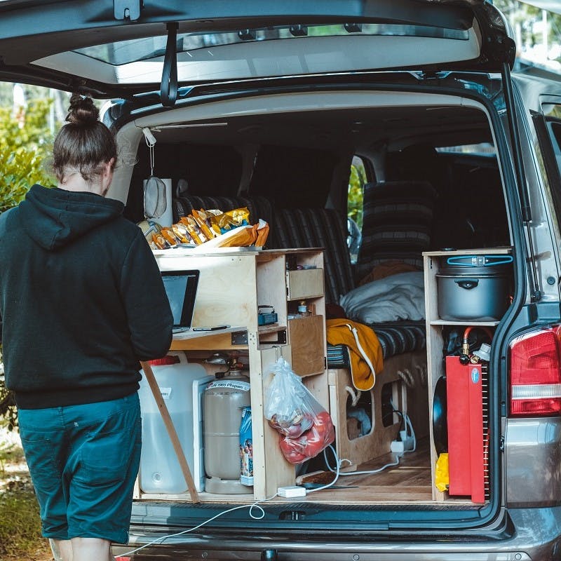 A girl works from her lap top from the back of her van life conversion.