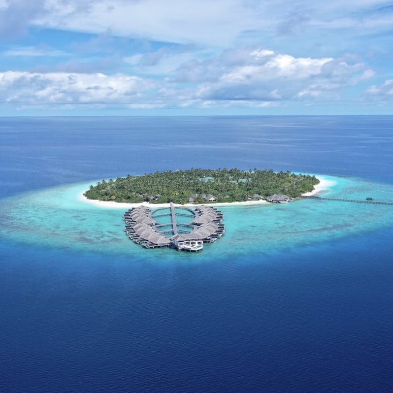An island in the Maldives is pictured from above in the middle of a vast blue ocean. 