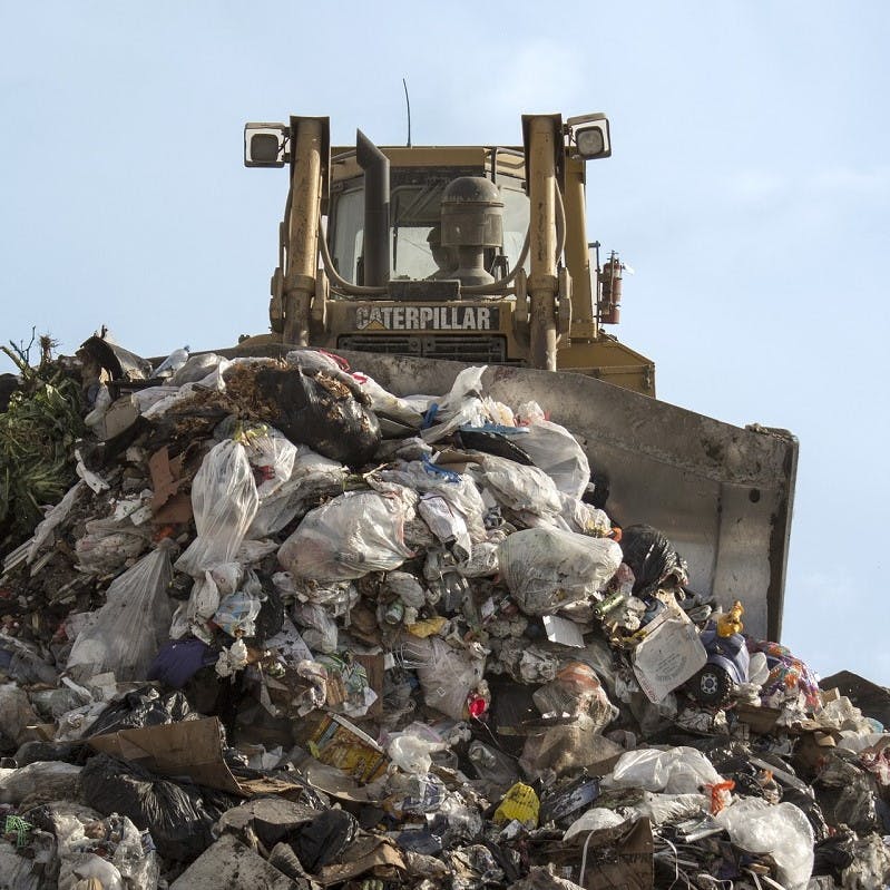 A digger pushing huge piles of waste across a toxic landfill site. Let's reduce, reuse, recycle our clothing to keep it out of landfill.