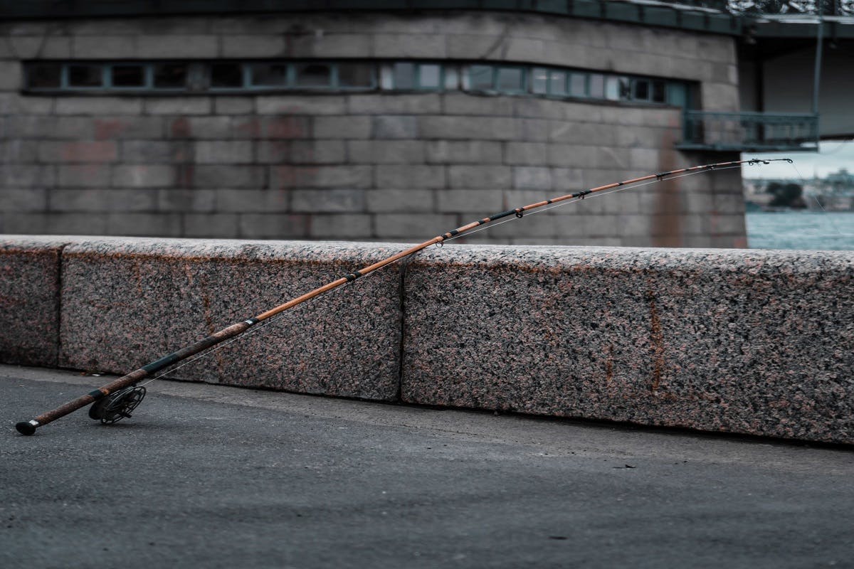 An unattended fishing rod rests against a wall of a waterway.