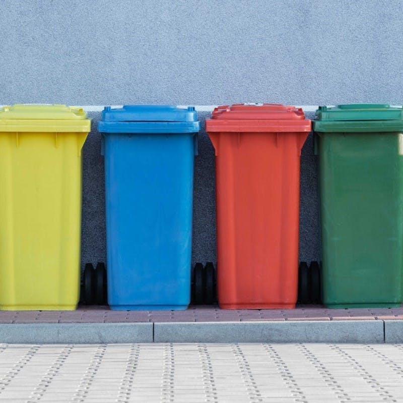 Four colorful recycling bins side by side on a sidewalk. 