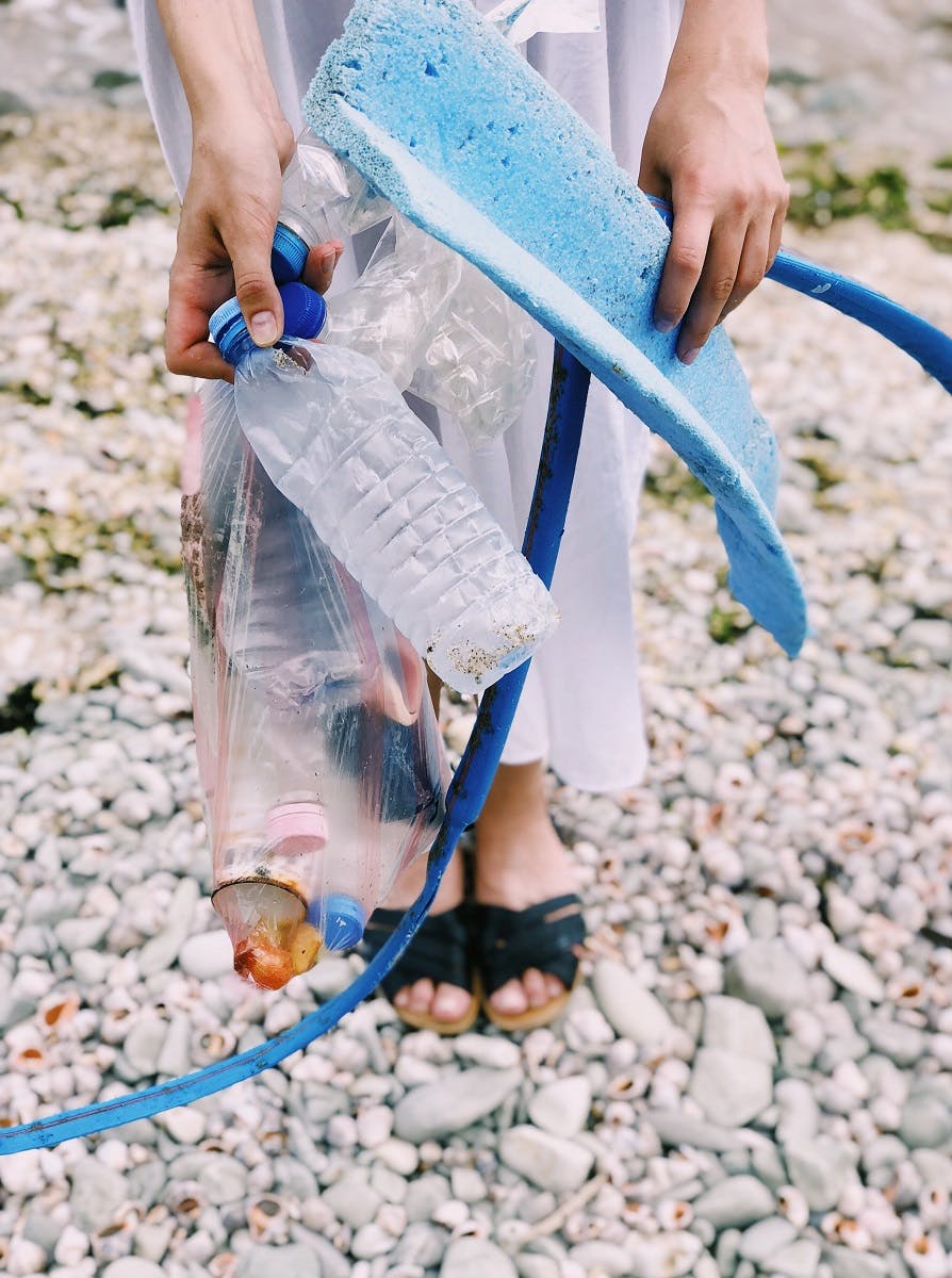 A lady on a beach with plastic waste that she has collected. 