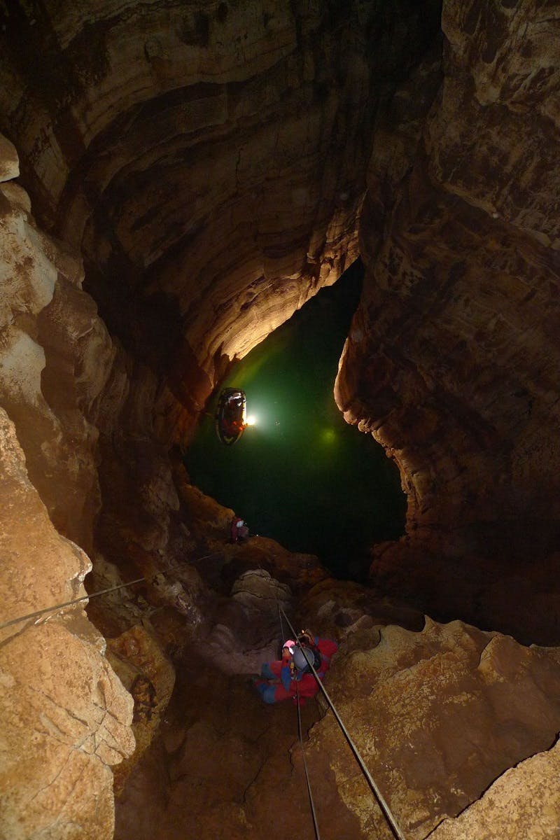 Cavers explore a cave with head torches and submerged in water up to waist-height 