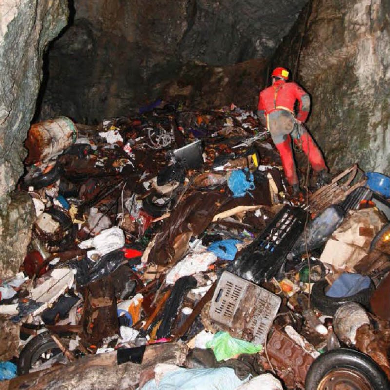 A caver in a full red suit and helmet abseils over a huge pile of solid waste inside Rupečica cave. Photo credit: PROTEUS project team.