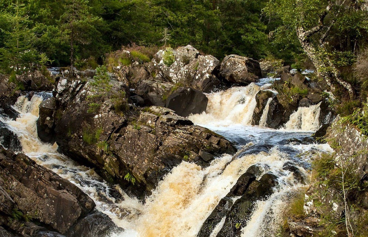 Water flows along a wooded river in Scotland