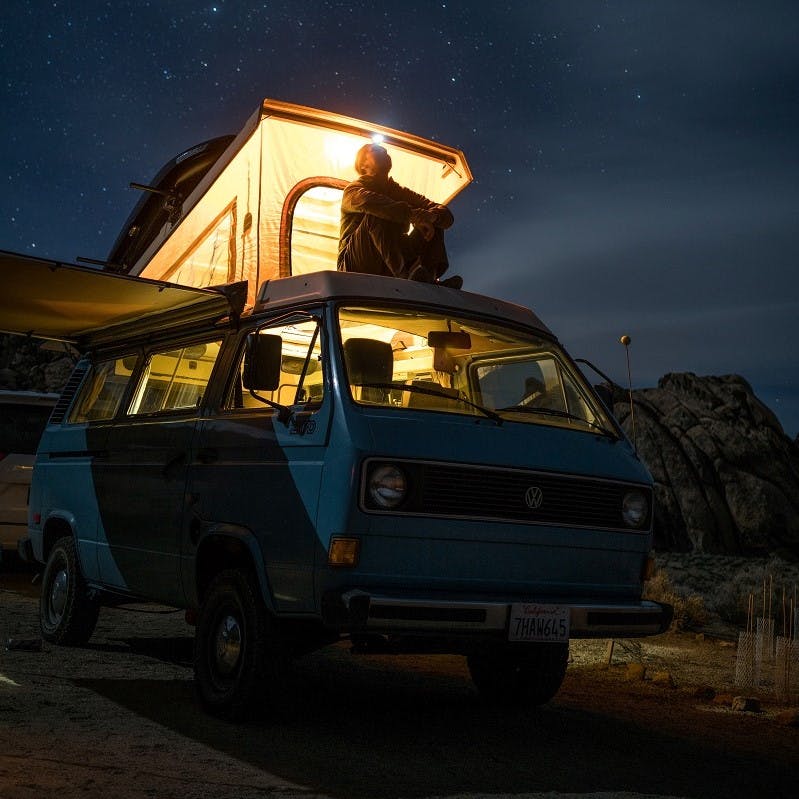 A man enjoying the nights sky from the roof of his remotely parked camper van.