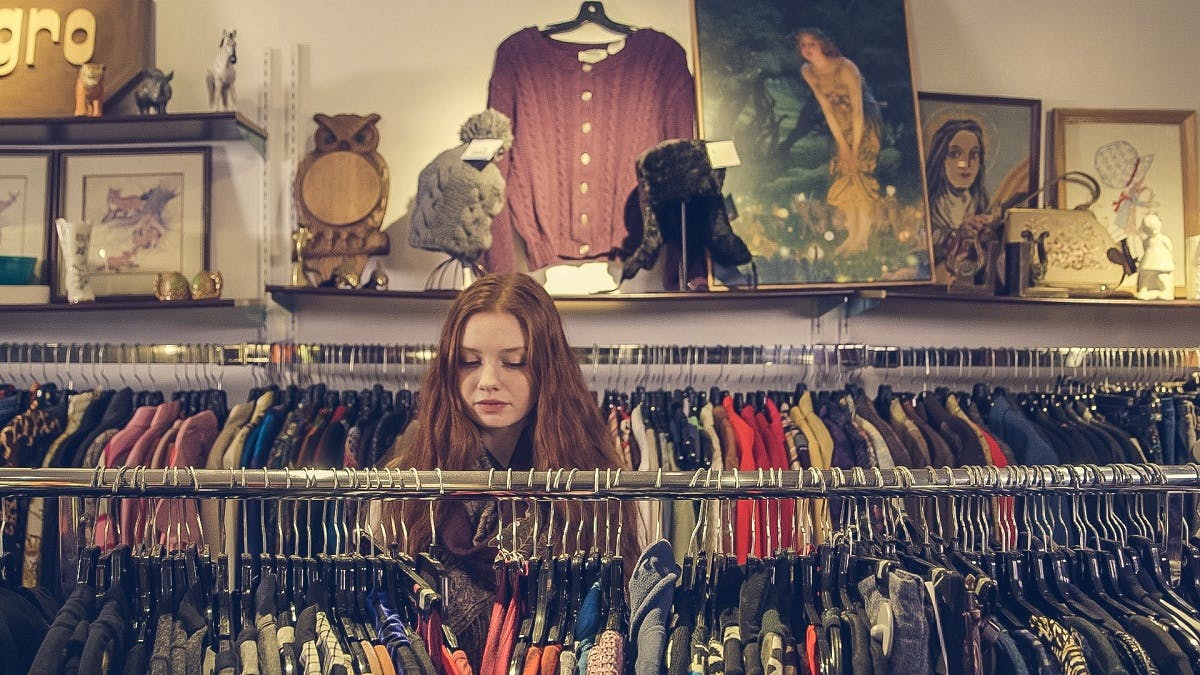 A girl browsing for clothing in a second hand shop. Shun fast fashion by purchasing second hand garments.