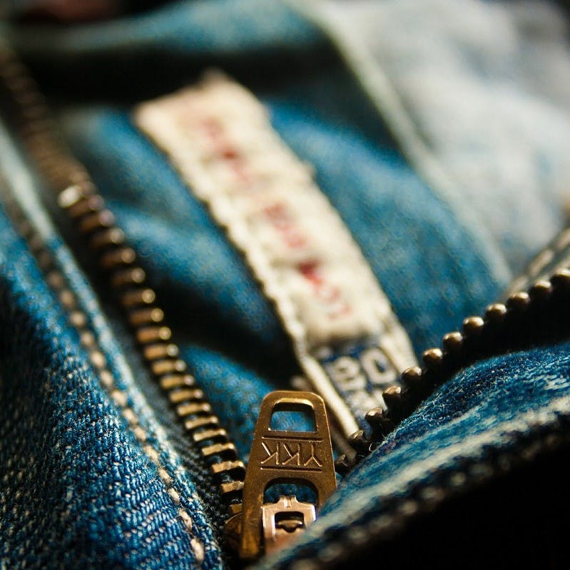 A close up photo of a YKK zip on a pair of blue jeans. Look for these signs of quality when trying to avoid fast fashion.