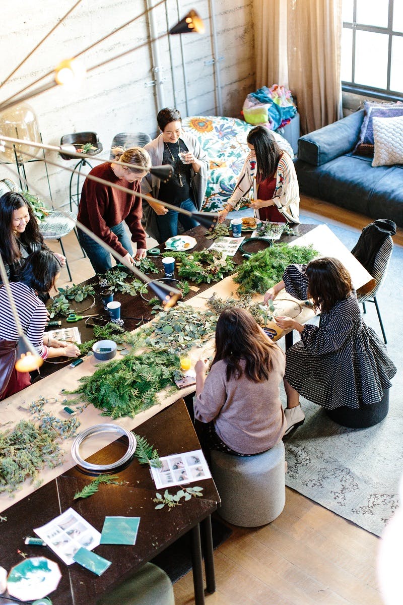 A group of friends gathered round a dining table with an assortment of leaves spread across the table.