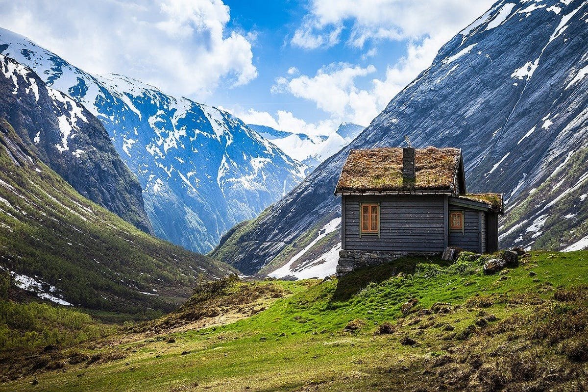 A house with a grass roof faces a mountain range. Eco houses, like nature, adapt to their environment.