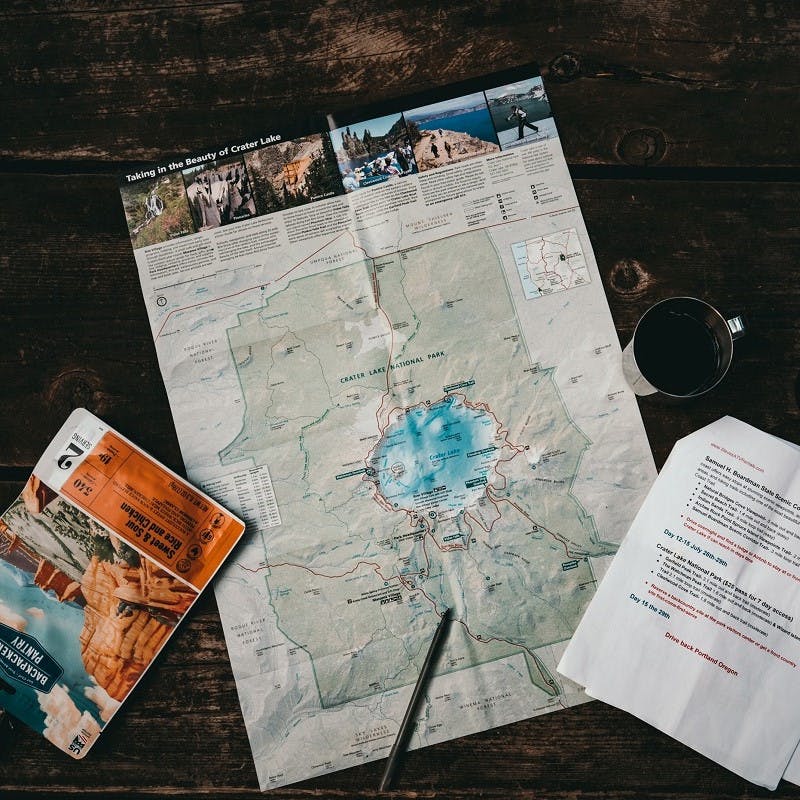 A map, a pen, a set of notes and a cup of coffee set out on a table as someone plans a travel without flying trip. 