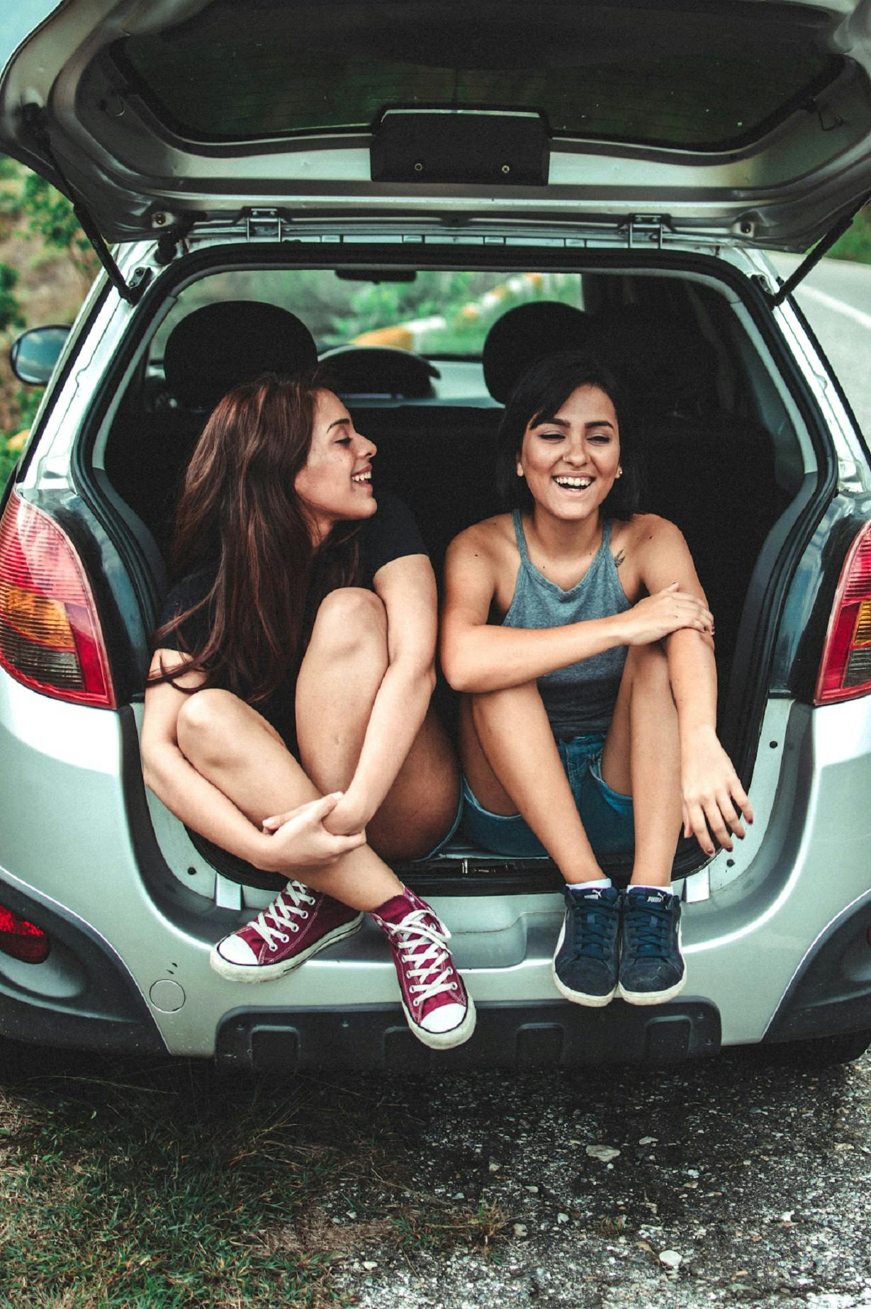 Two girls sat in the boot of their car chatting. Travelling without flying means more roadtrips!