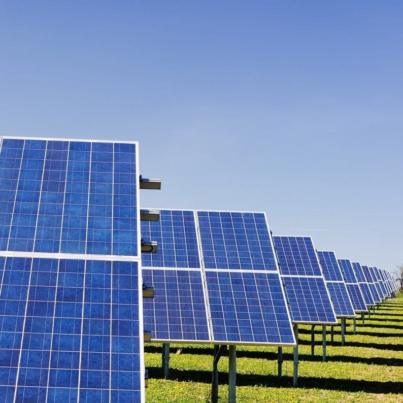 Aerial photo of a solar farm with solar panels layed out over green grass. 