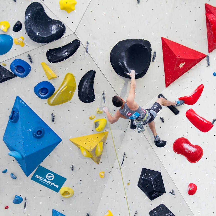 Climber lead climbing on an indoor climbing gym with colourful holds. 