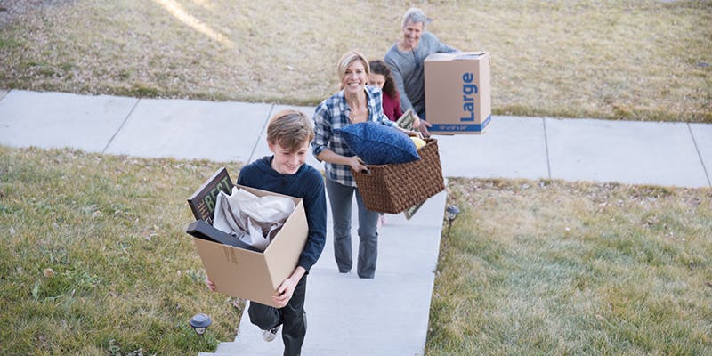 A family moving during the spring housing market. They are carrying boxes up the stairs of a house.