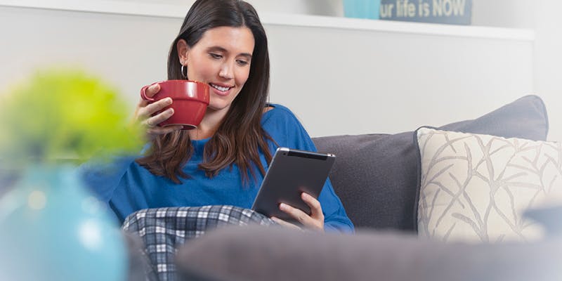 Women sitting on her couch, furniture thrifting on a tablet