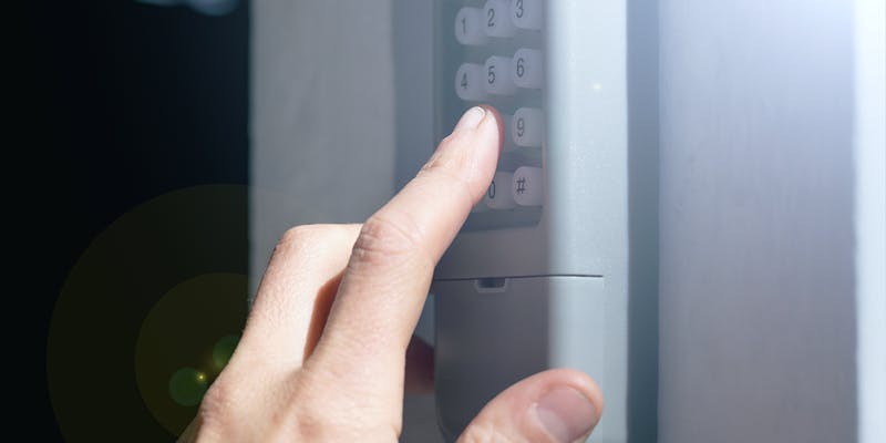 A person learning how to program a garage door keypad. It is a close-up of their hand pressing buttons on the keypad.