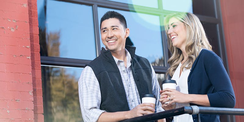 A couple standing in front of a townhouse, drinking coffee