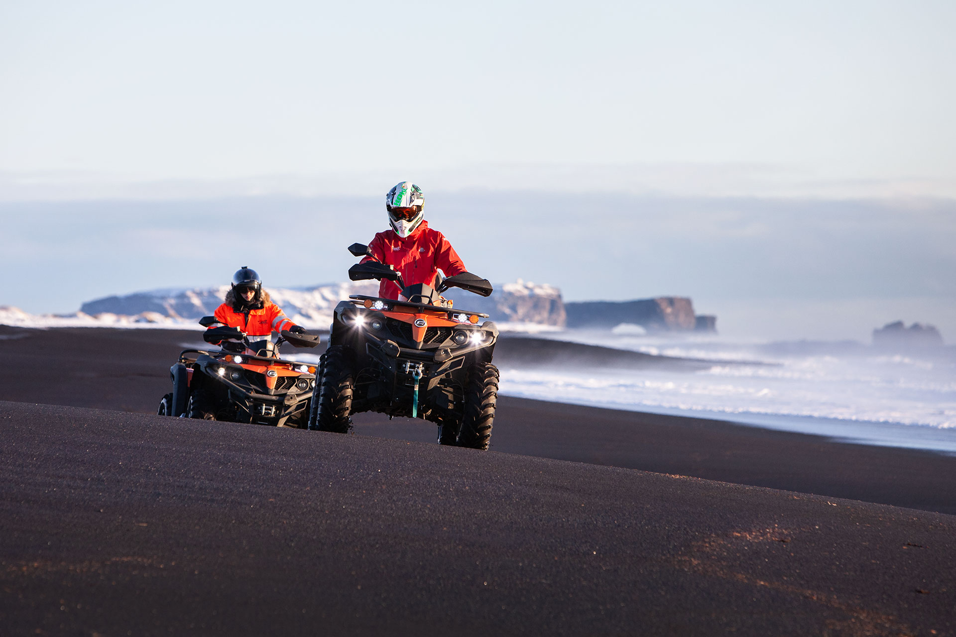 Two men dressed in red on an ATV tour on a black beach in Iceland