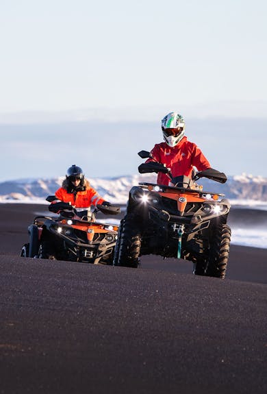 Two men dressed in red on an ATV tour on a black beach in Iceland