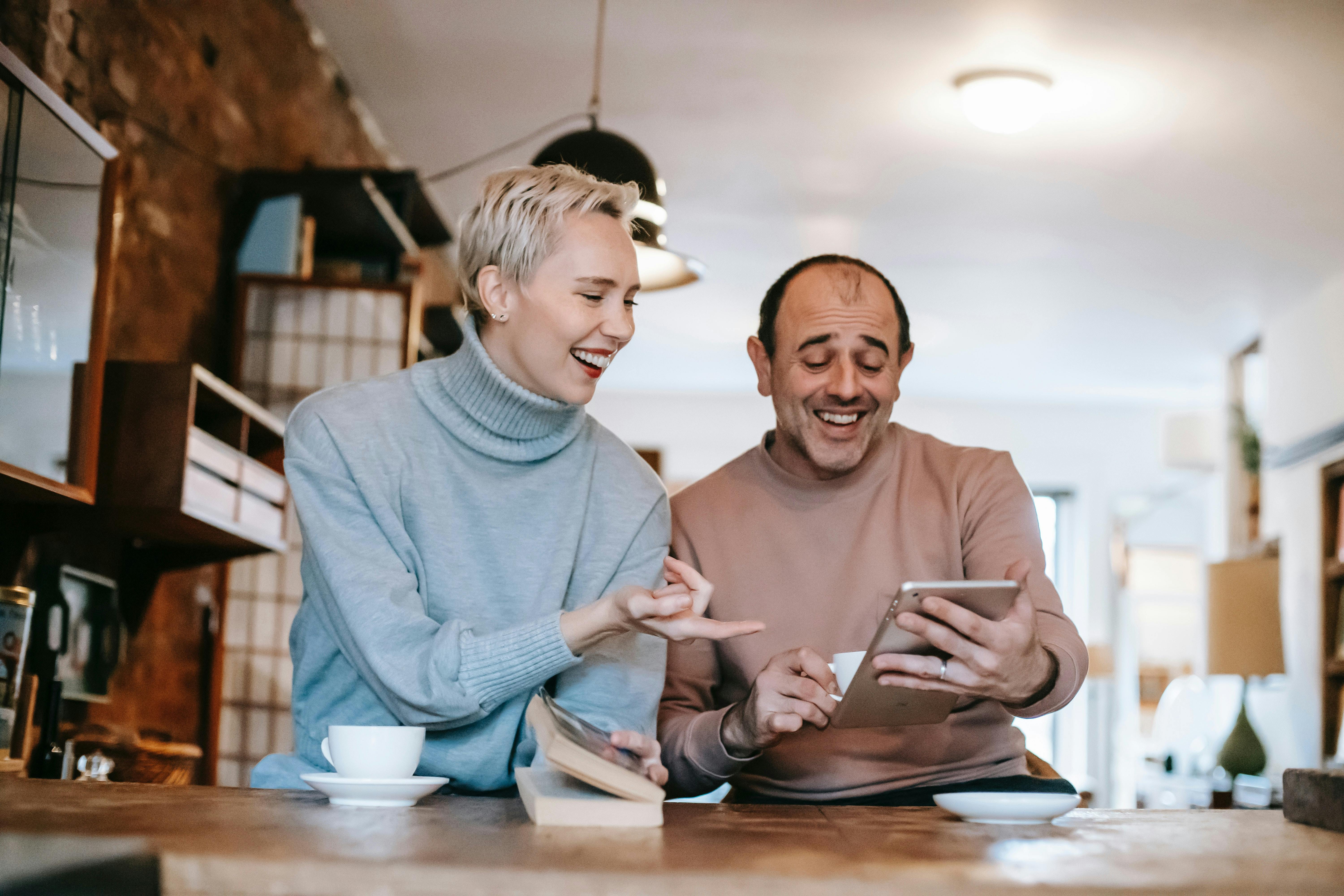 Blond woman and dark hair man smiling down at the man's tablet