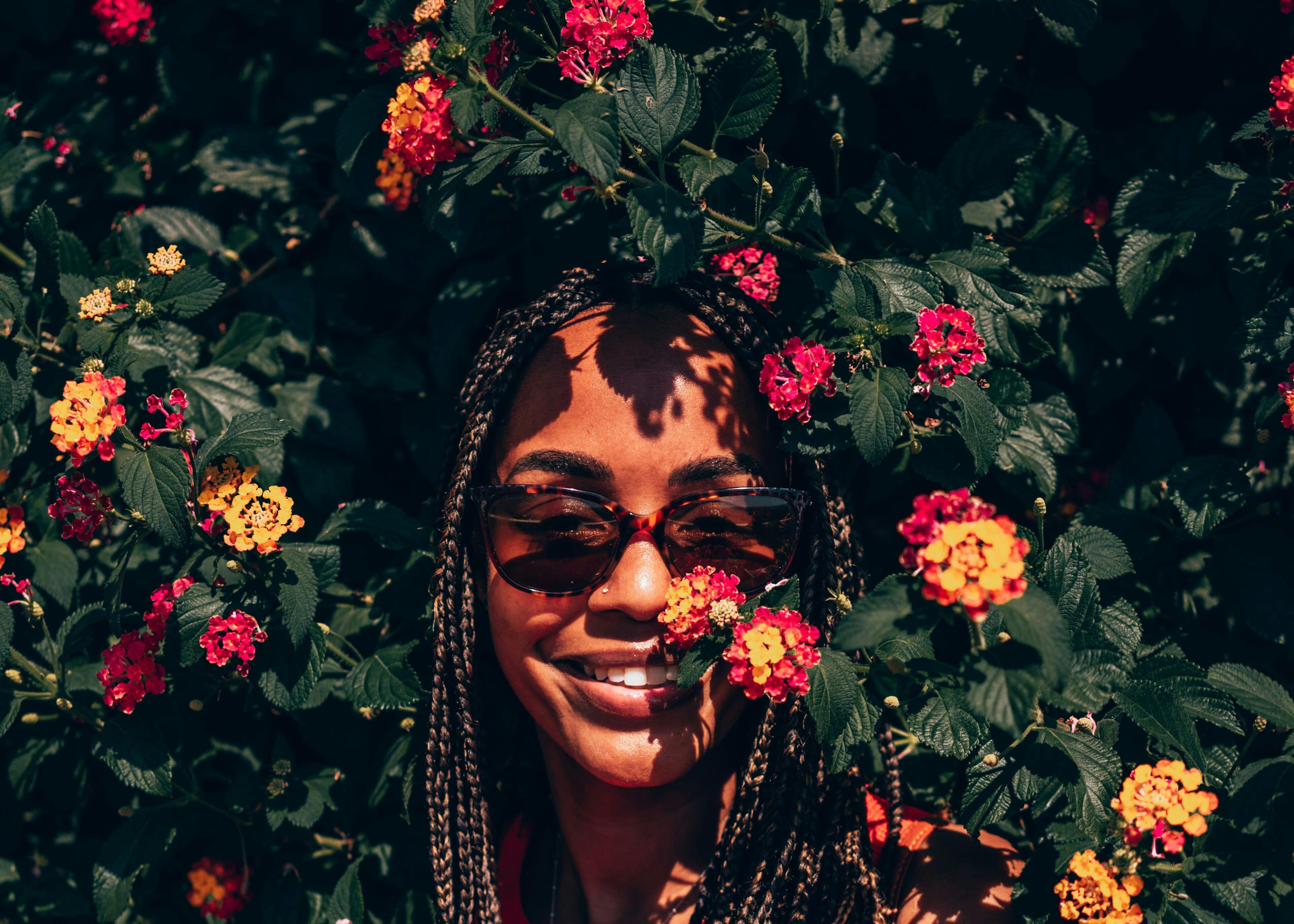 Mulher usando óculos de sol espiando por trás de arbusto florido vibrante e bonito.
