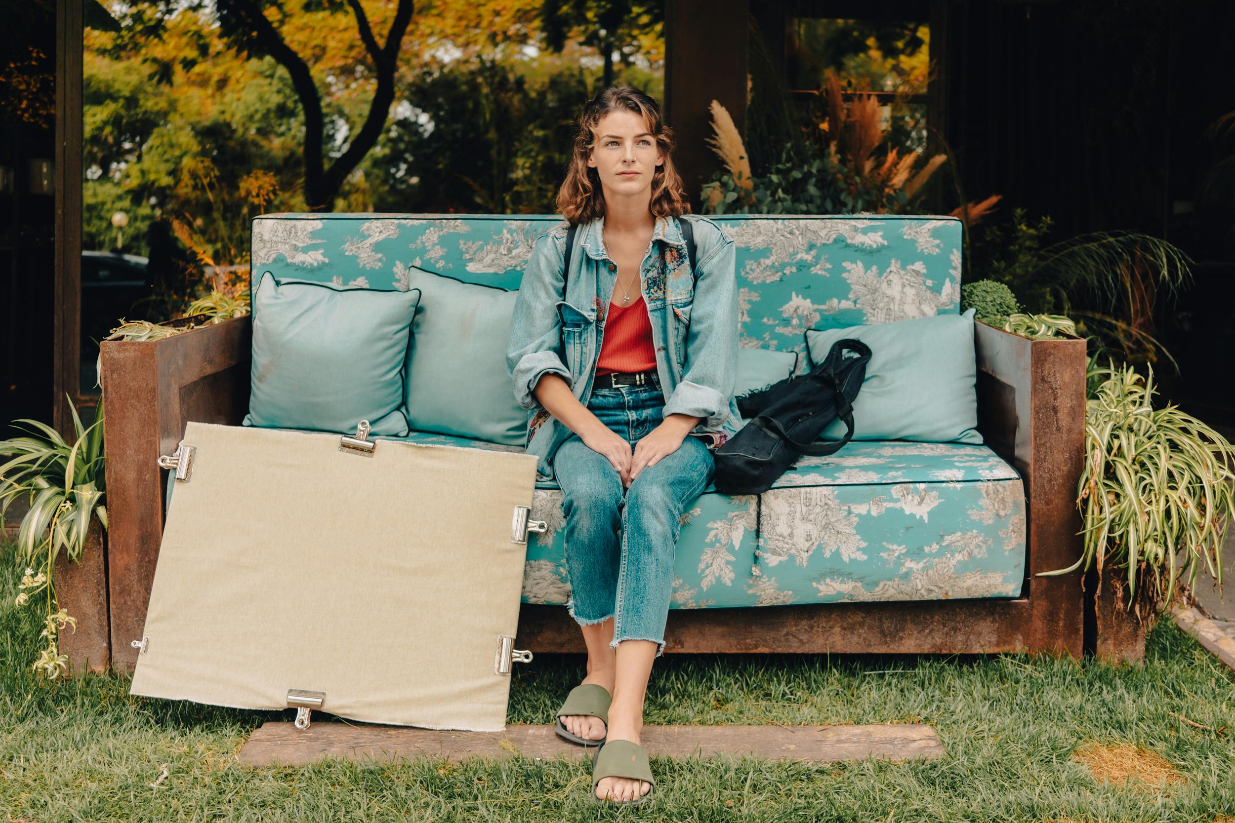 Tanya sits on a sofa, with her canvas resting on the floor to her right.