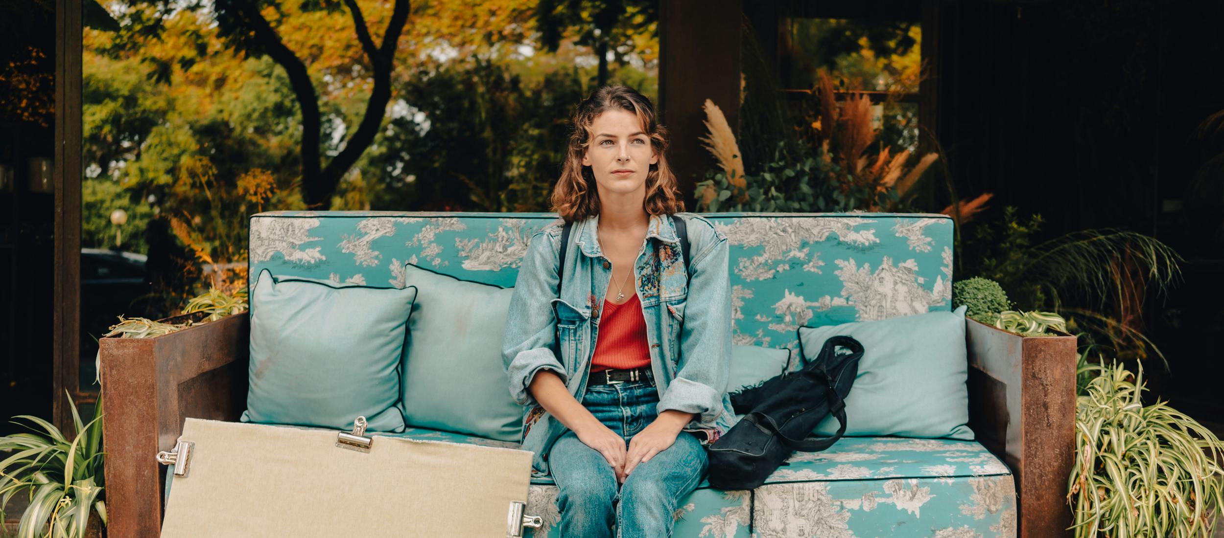Tanya sitting in a blue flowered sofa with a painting by her side