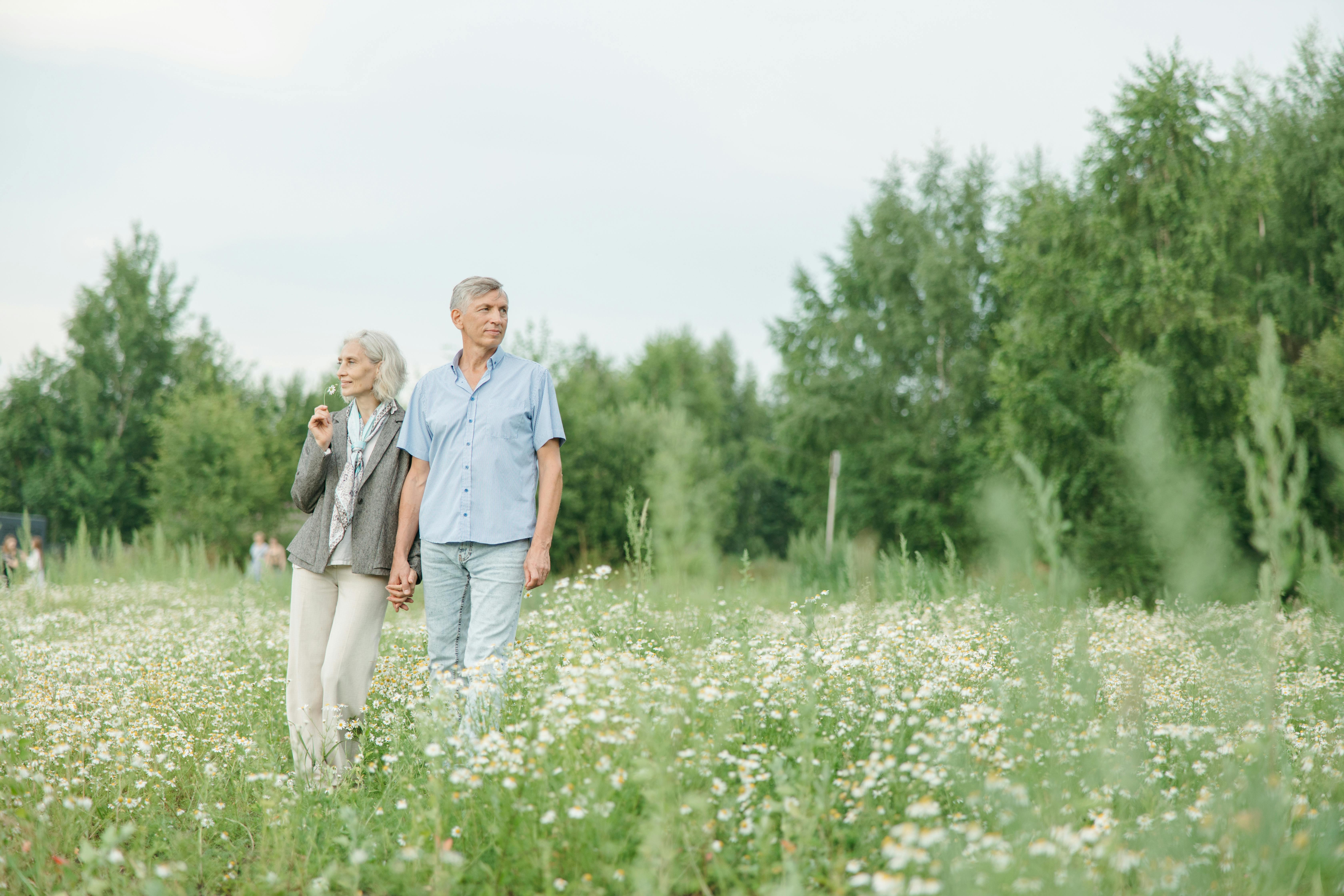 A retiree couple holding hands while standing in a lush, flower-filled field, conveying a sense of peace and companionship in their golden years.