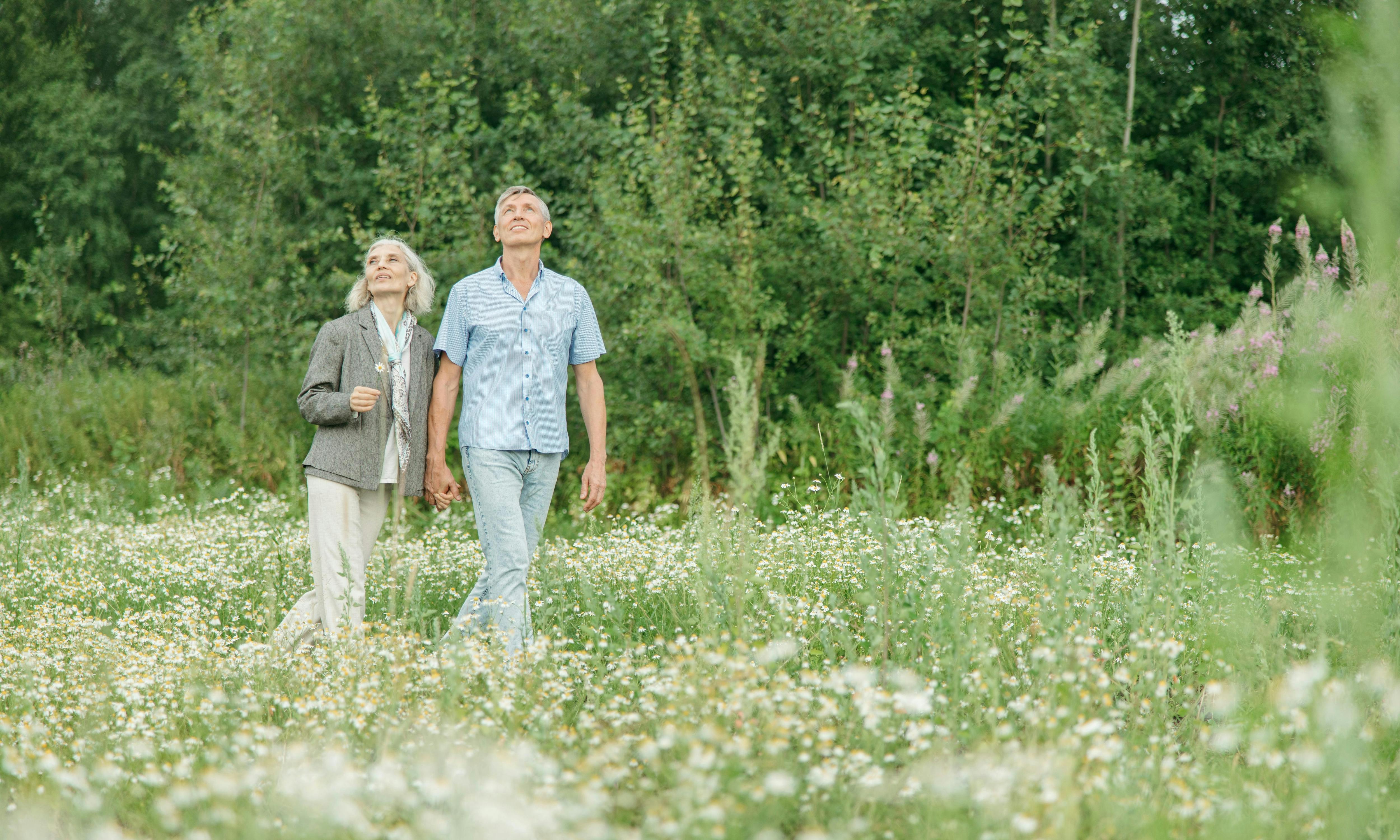 A retiree couple holding hands while standing in a lush, flower-filled field, conveying a sense of peace and companionship in their golden years.
