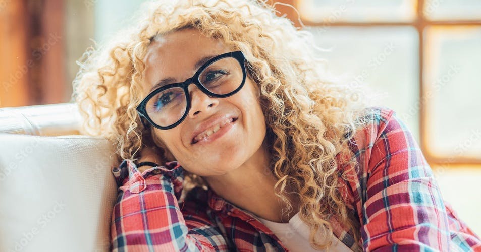 Cheerful young adult pretty middle age woman eyewear portrait having fun and smiling at home in bright living room. Happy female people enjoy indoor resting activity on the sofa and wearing eyeglasses