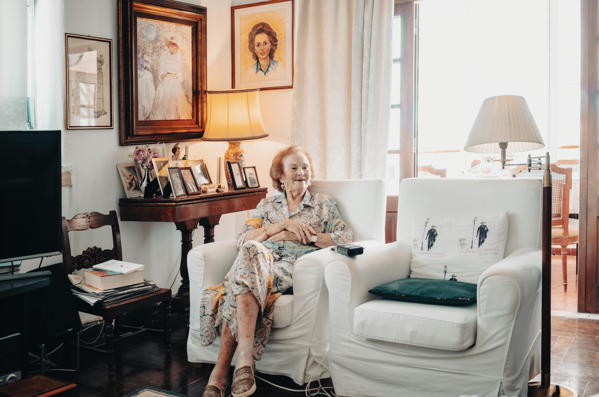 An older woman sitting on her house's white sofa, looking left and smiling