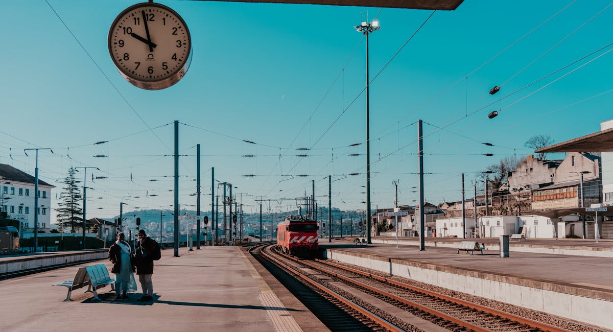 Trem chegando à estação Porto - Campanhã com um casal parado na plataforma, sob um relógio suspenso marcando 9h56.