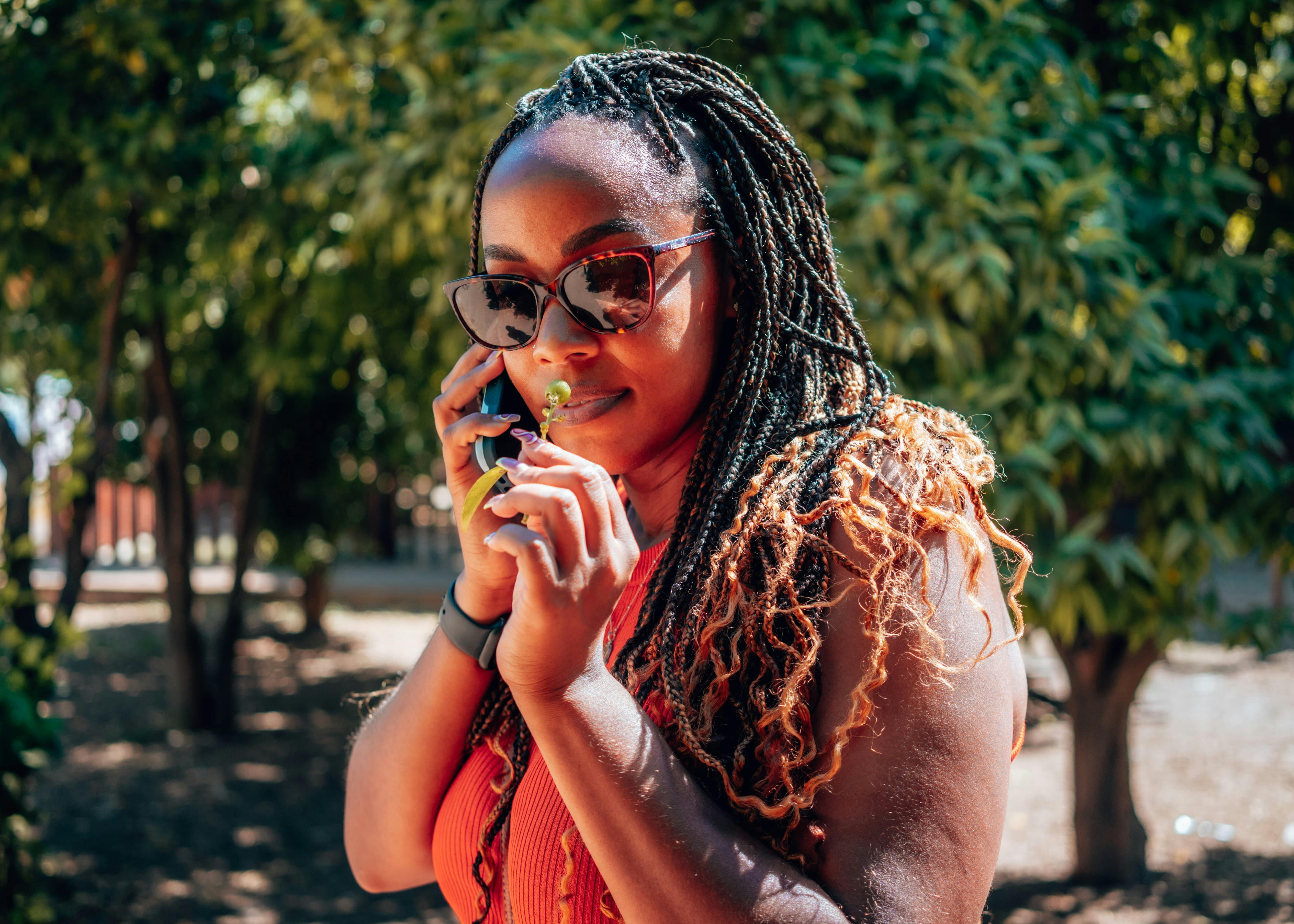 Woman on the phone, pausing to smell a delicate flower blossom