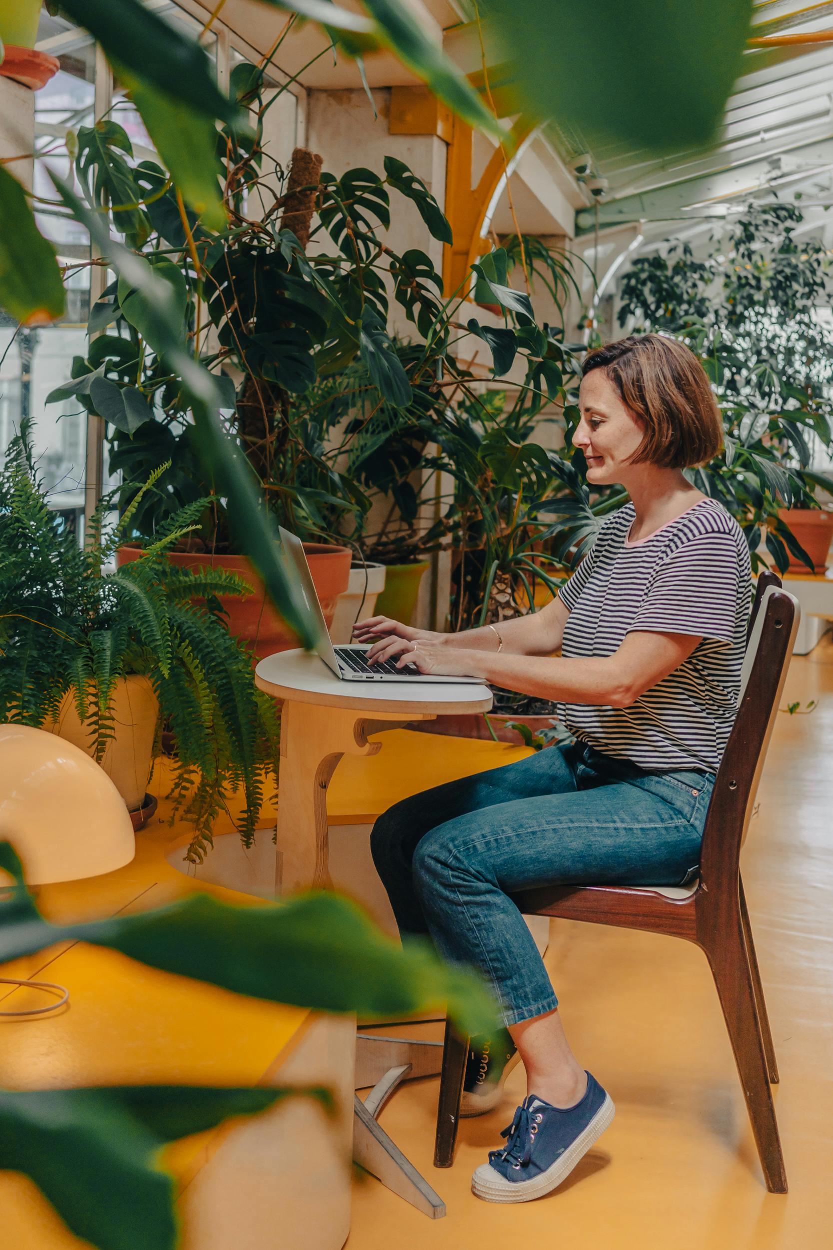 Woman sitting on a chair and writing on her laptop, surrounded by vased plants