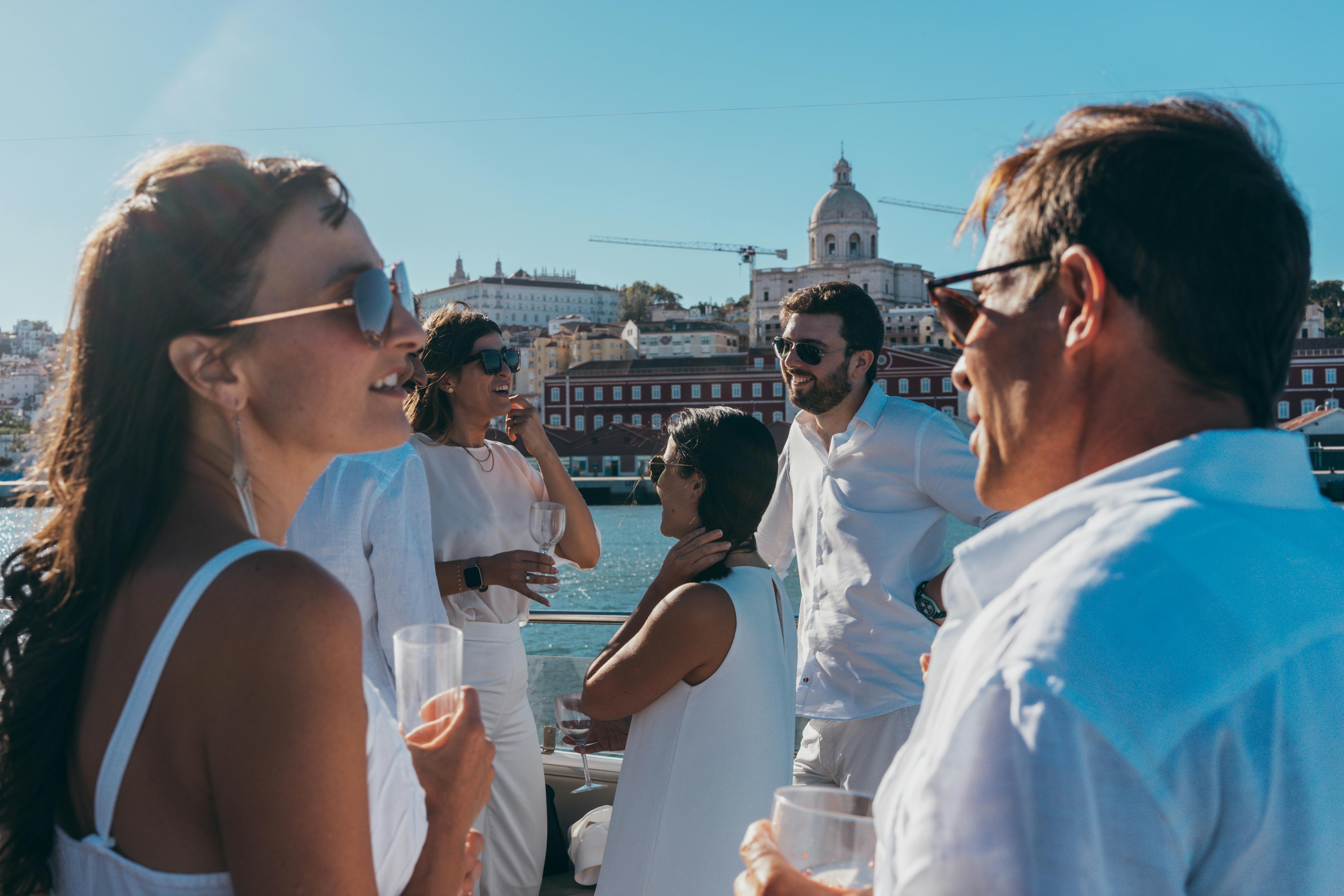 six people dressed in white with sunglasses and a drink in hand, talking close to a river
