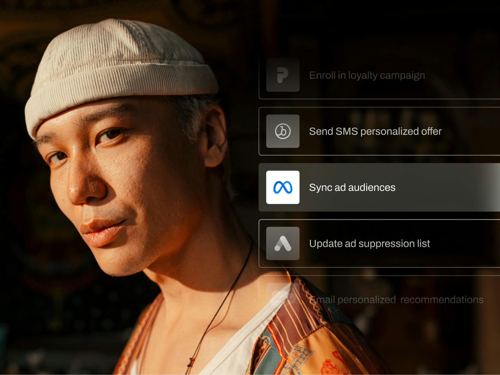 A man wearing a cream-colored knit cap and patterned shirt looks toward the camera in warm, dramatic lighting. Overlaid on the right are digital marketing actions in a user interface, with "Sync ad audiences" highlighted among other options like "Send SMS personalized offer" and "Update ad suppression list." The image conveys targeted advertising or audience segmentation workflows in a marketing automation setting.