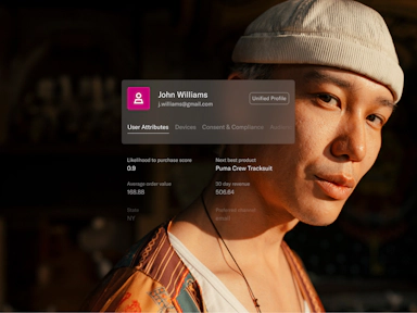 A young man wearing a patterned jacket and a light beige knit cap gazes confidently at the camera in warm sunlight. Overlaid on the image is a digital customer profile card for “John Williams” with an email address and tabs like “User Attributes” and “Devices.” Key metrics shown include a high purchase likelihood score of 0.9, average order value of $168.88, and a suggested next product—Puma Crew Tracksuit. Additional details note a 30-day revenue of $506.64 and preferred communication channel as email. The image illustrates the use of detailed user data to drive relevant marketing recommendations.