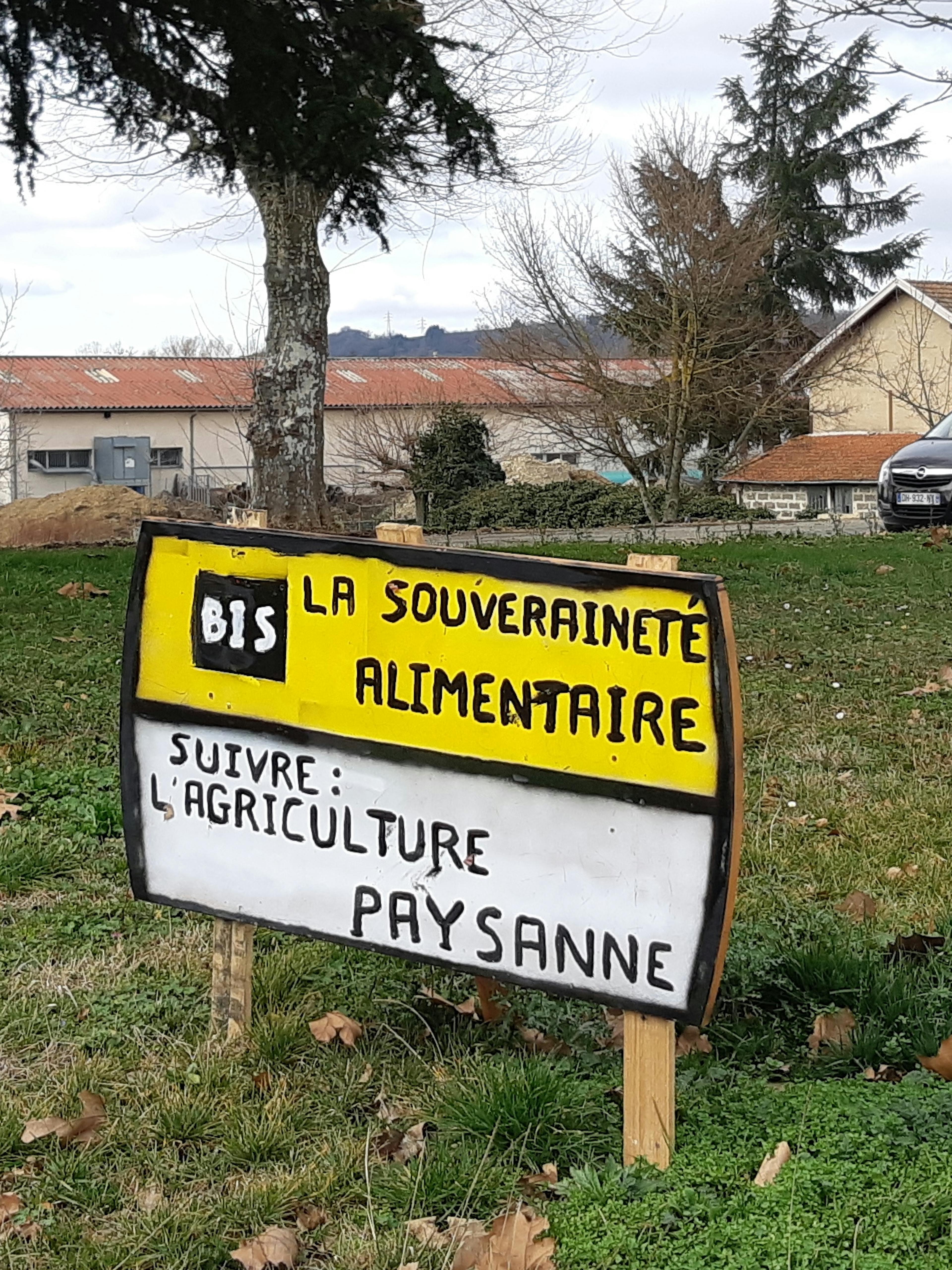 sur un rond point, un faux panneau de circulation portant la mention "La souveraineté alimentaire : suivre l'agriculture paysanne"