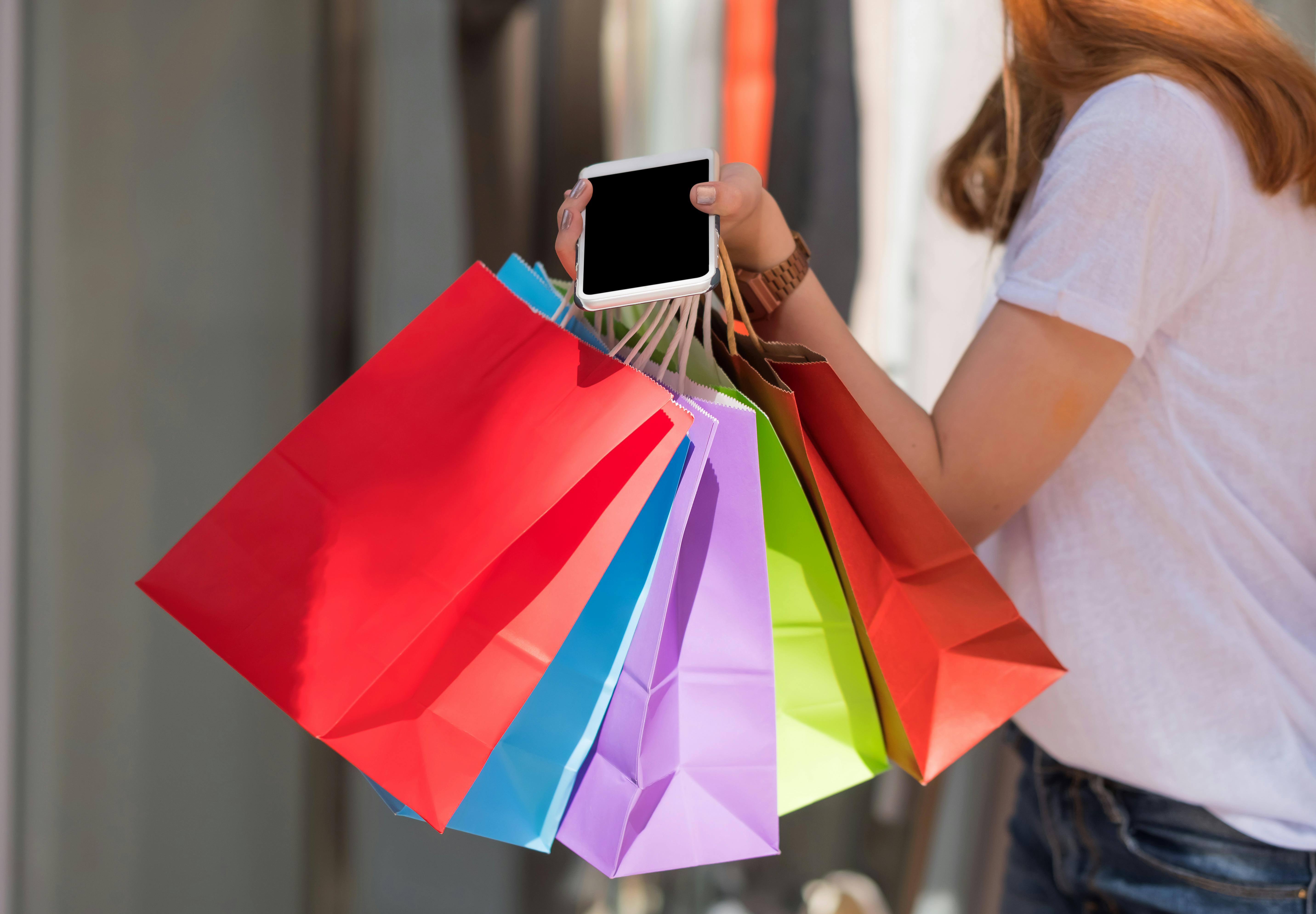 Femme tenant un téléphone intelligent et des sacs de shopping