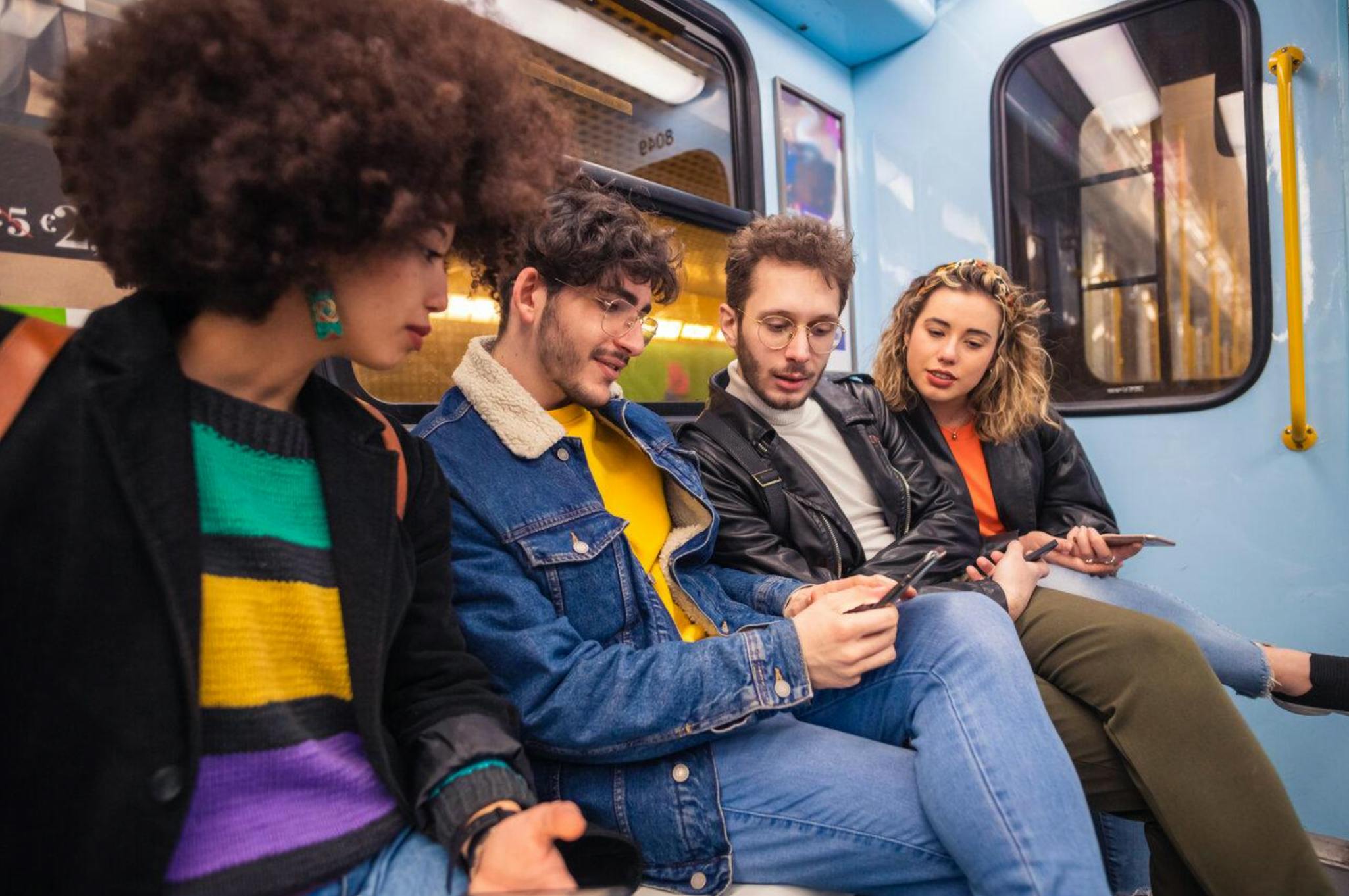 Groupe d'amis de quatre personnes voyageant dans le métro utilisant un smartphone accro aux tendances sociales et virales