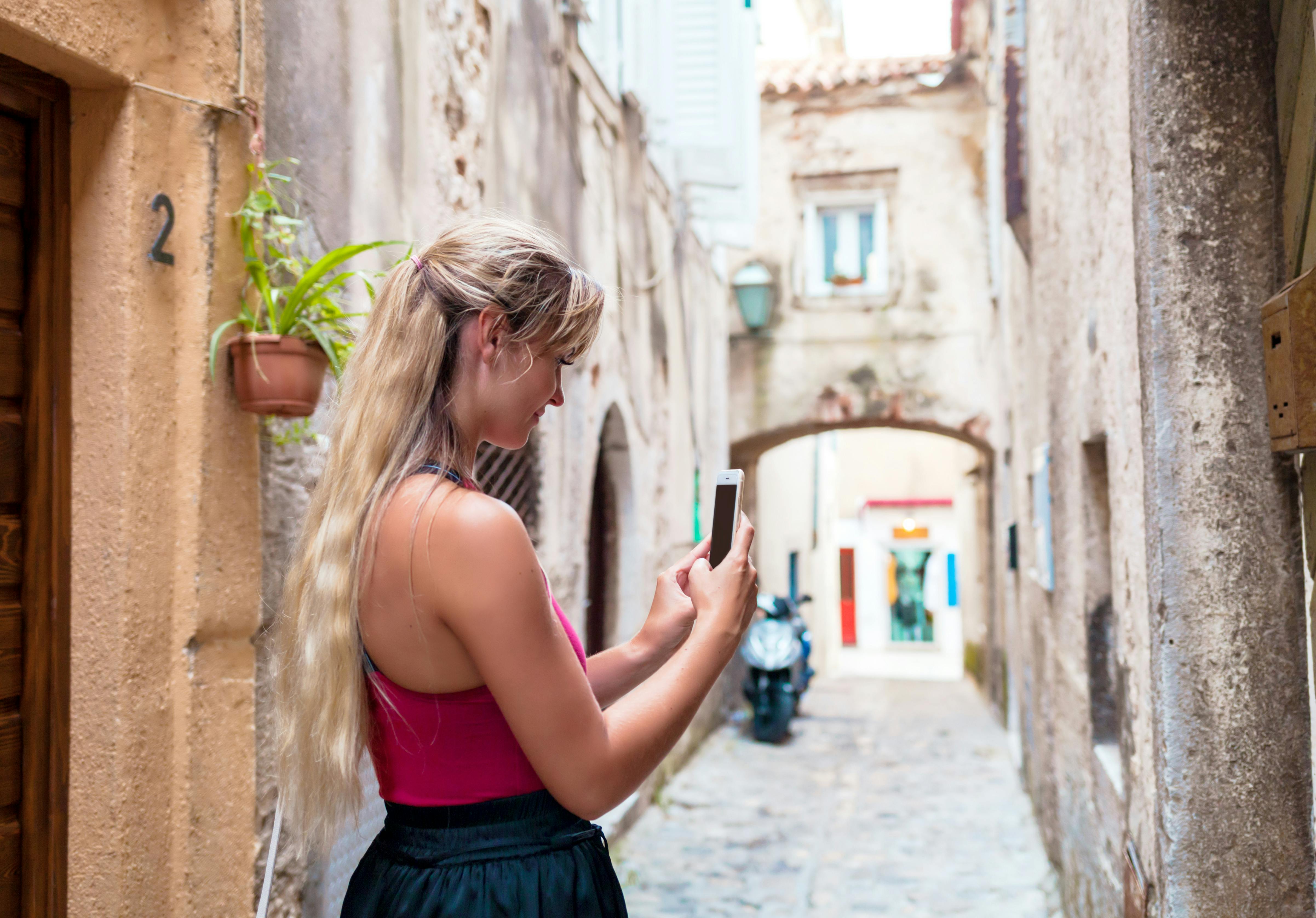 Une touriste prenant des photos en utilisant un téléphone mobile dans une vieille rue étroite en Croatie