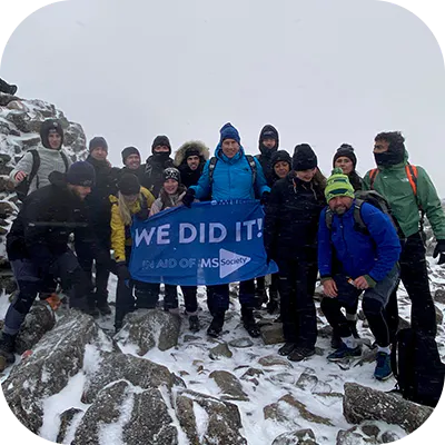 Charity climbers atop a snowy mountain with a sign that reads, "we did it".